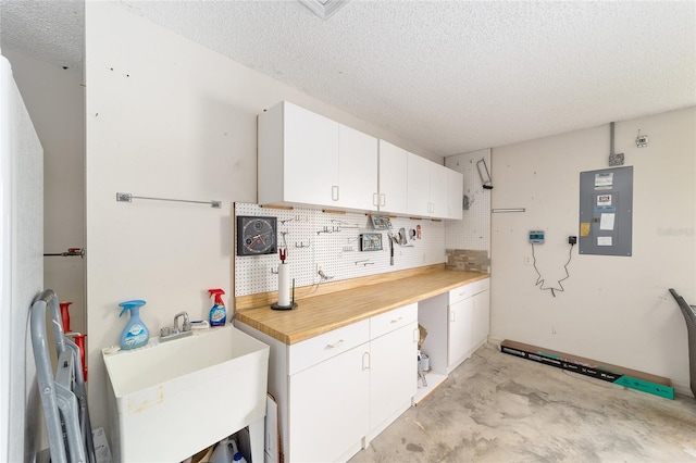 2608 Casso Ct, The Villages, FL 32162 - kitchen featuring electric panel, a textured ceiling, a sink, unfinished concrete flooring, and white cabinets