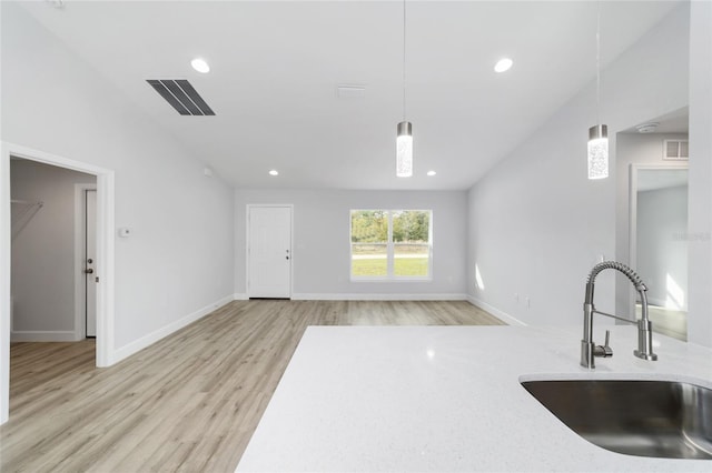 kitchen featuring a sink, light wood finished floors, hanging light fixtures, recessed lighting, and light stone countertops