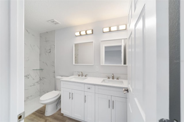 bathroom featuring toilet, double vanity, wood finished floors, and a marble finish shower