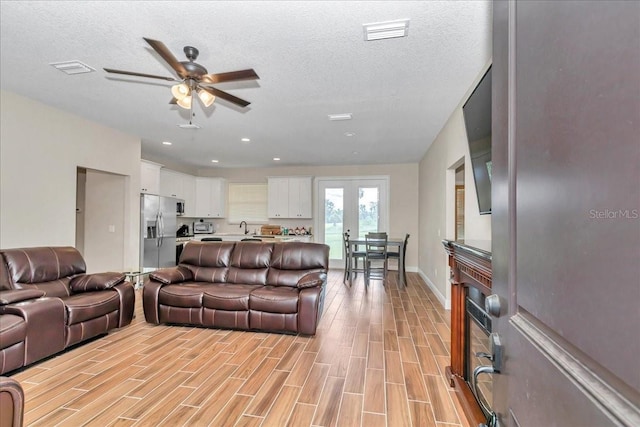 living area featuring ceiling fan, light wood-style floors, a textured ceiling, baseboards, and recessed lighting