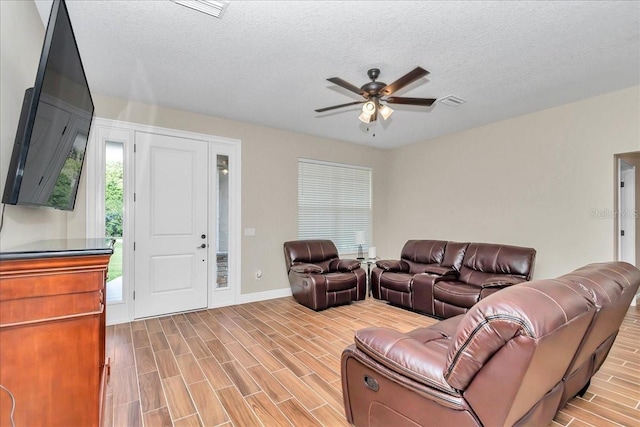 living room featuring a ceiling fan, wood finished floors, baseboards, and a textured ceiling