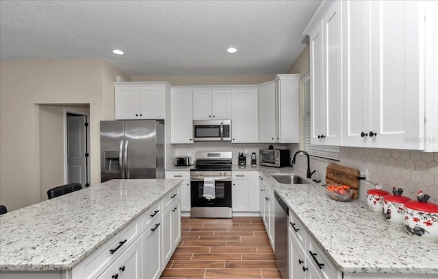 kitchen with stainless steel appliances, a sink, white cabinets, a kitchen island, and recessed lighting