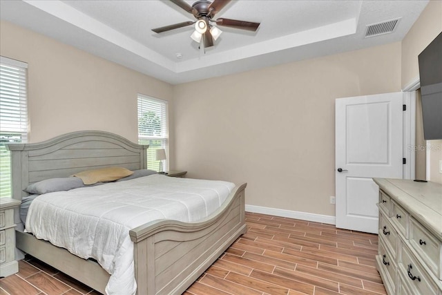 bedroom featuring a raised ceiling, baseboards, light wood-type flooring, and ceiling fan