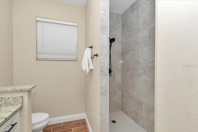 full bathroom with a tile shower, baseboards, vanity, wood finish floors, and toilet