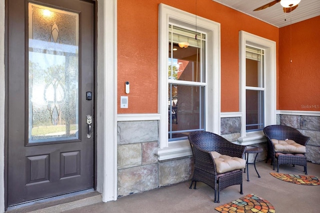 view of exterior entry with stone siding, a ceiling fan, and a porch