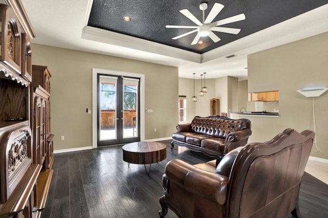living area with a tray ceiling, ceiling fan, baseboards, french doors, and wood-type flooring