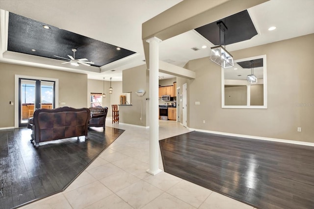living area featuring a raised ceiling, ceiling fan, decorative columns, baseboards, and wood finished floors