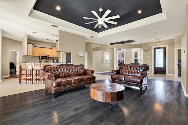 living room with a raised ceiling, a ceiling fan, baseboards, crown molding, and recessed lighting