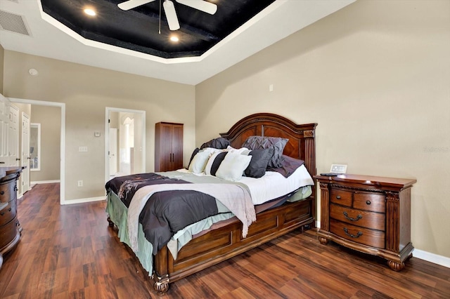 bedroom with wood finished floors, a tray ceiling, baseboards, and a ceiling fan