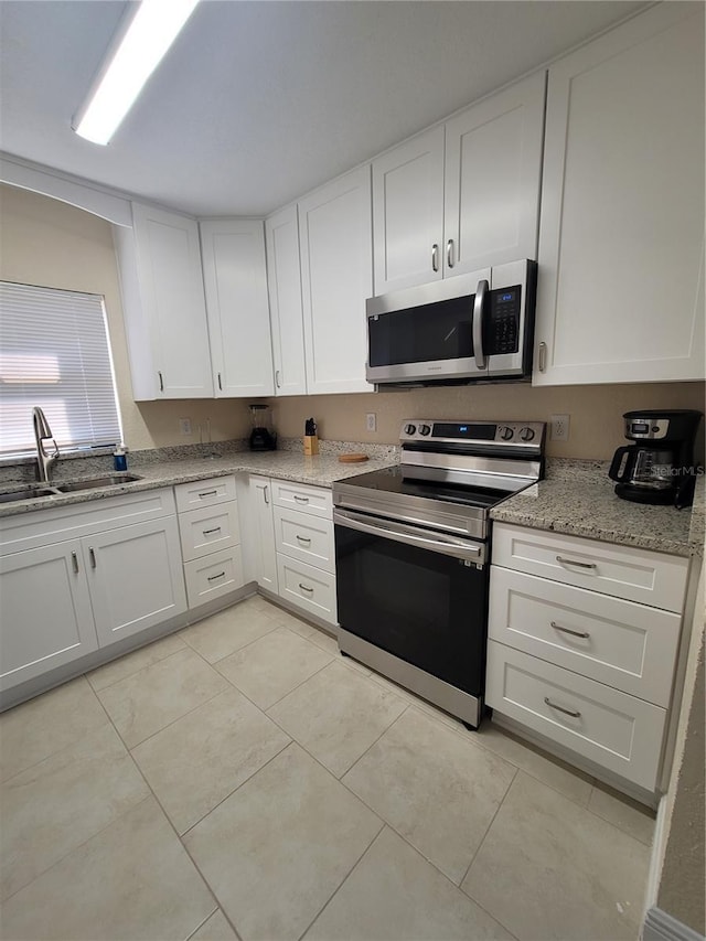 kitchen featuring appliances with stainless steel finishes, a sink, white cabinets, light tile patterned flooring, and light stone countertops