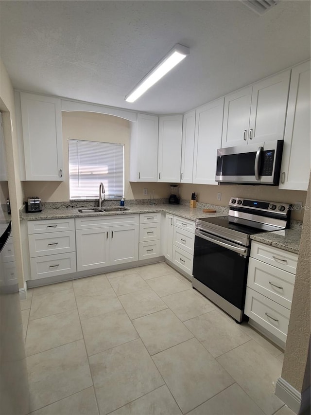 kitchen featuring stainless steel appliances, a sink, white cabinetry, and light stone countertops