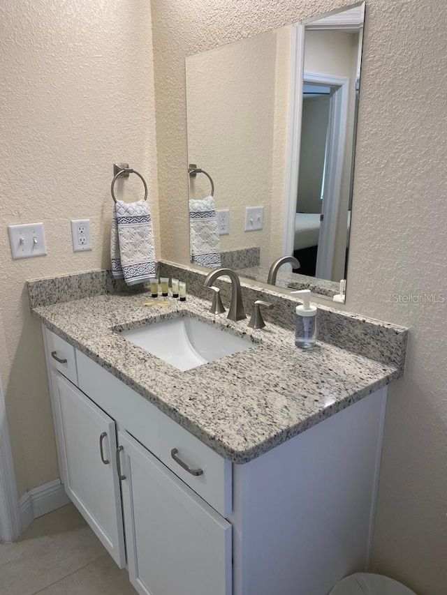 bathroom with a textured wall, vanity, and tile patterned flooring