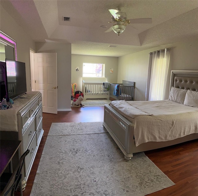 bedroom featuring a raised ceiling, dark wood-style flooring, a textured ceiling, and baseboards