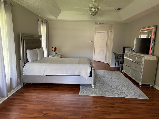 bedroom featuring a tray ceiling, dark wood-style flooring, baseboards, and a ceiling fan
