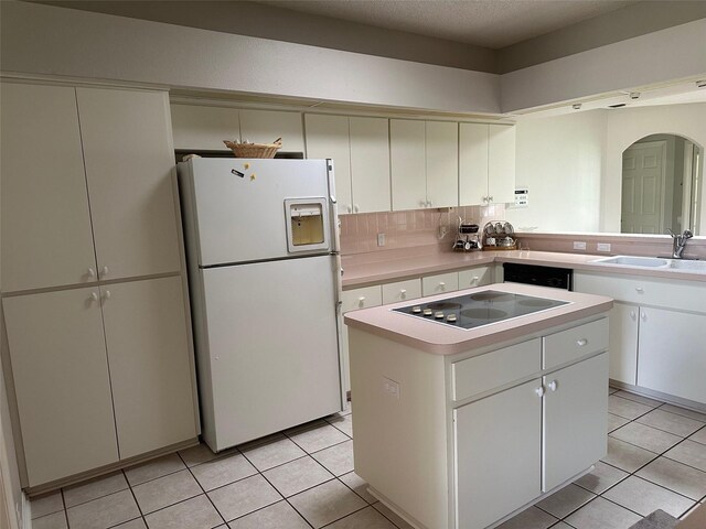 kitchen featuring freestanding refrigerator, black electric stovetop, a kitchen island, a sink, and light tile patterned floors