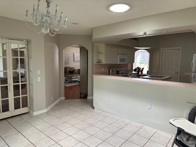 kitchen with white microwave, arched walkways, electric range oven, a textured ceiling, and light tile patterned flooring