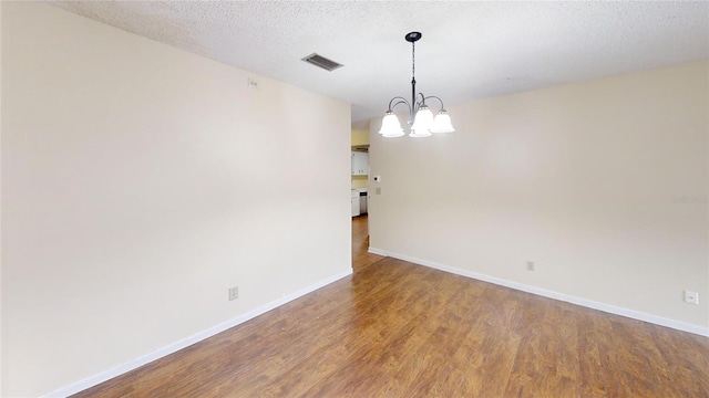 spare room featuring wood finished floors, a chandelier, baseboards, and a textured ceiling