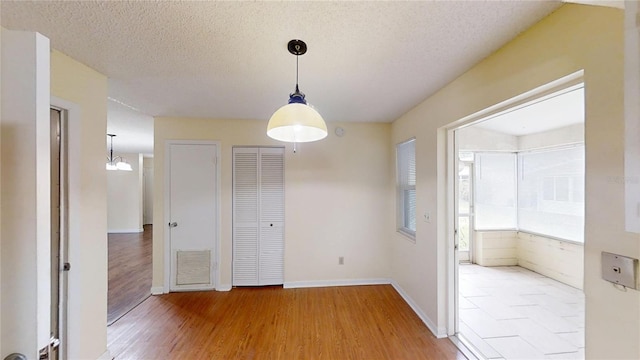 unfurnished dining area featuring light wood-type flooring, a textured ceiling, and baseboards