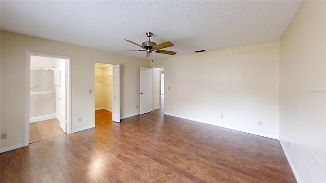 unfurnished bedroom with wood finished floors, a walk in closet, connected bathroom, baseboards, and a textured ceiling