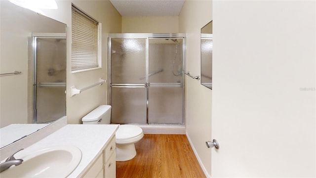 bathroom with a shower stall, wood finished floors, vanity, and toilet