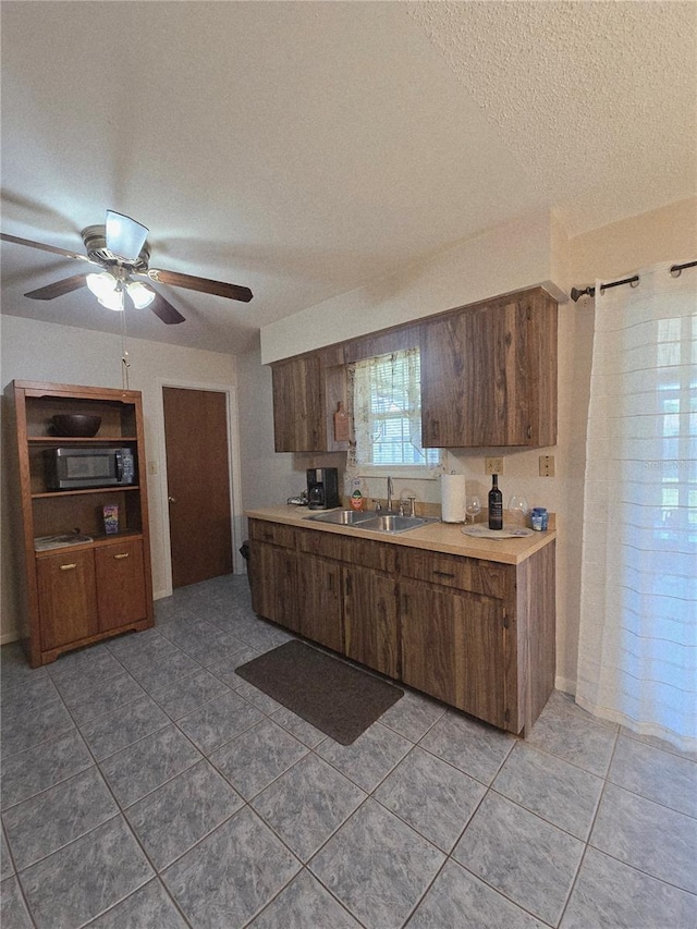 kitchen featuring a sink, light countertops, a textured ceiling, light tile patterned floors, and a ceiling fan