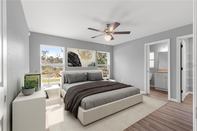bedroom with light wood-style floors, ceiling fan, ensuite bathroom, and baseboards