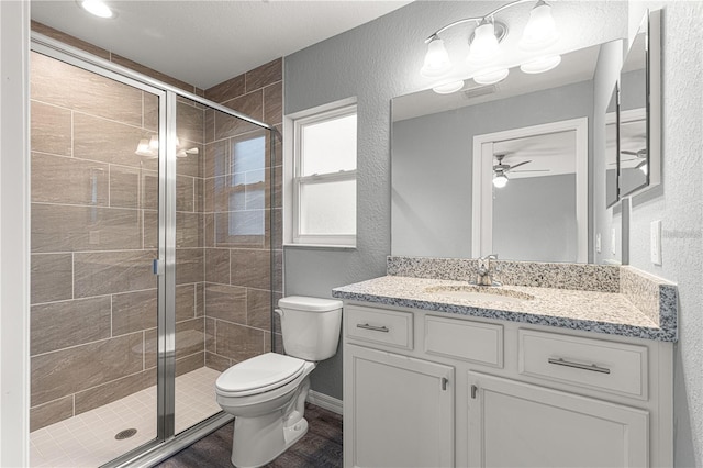 bathroom featuring ceiling fan, a textured wall, a stall shower, toilet, and vanity