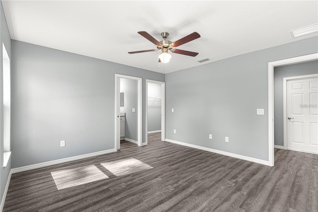 unfurnished bedroom with dark wood-type flooring, baseboards, a walk in closet, and a ceiling fan