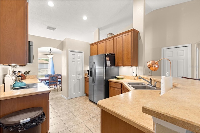 kitchen with stainless steel appliances, a sink, a peninsula, brown cabinetry, and light countertops