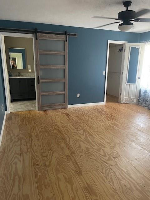 6051 NE 25th Ave, Ocala, FL 34479 - unfurnished bedroom featuring a barn door, wood finished floors, a spacious closet, baseboards, and ceiling fan