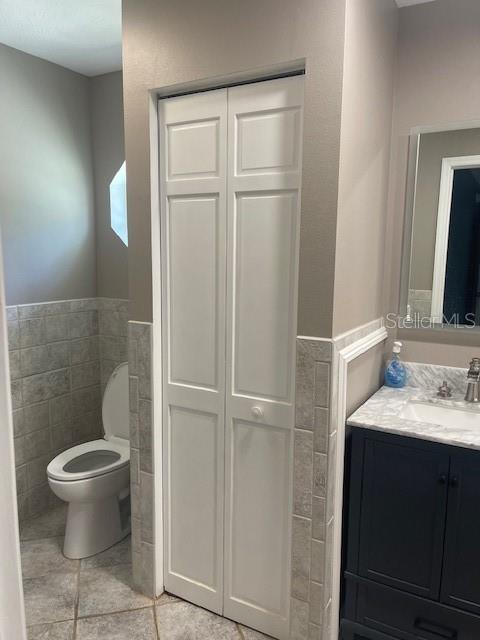 6051 NE 25th Ave, Ocala, FL 34479 - bathroom featuring a closet, toilet, a wainscoted wall, vanity, and tile walls