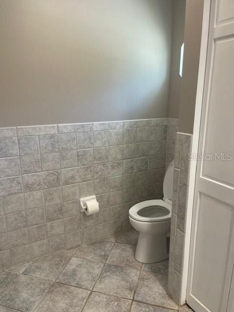 6051 NE 25th Ave, Ocala, FL 34479 - bathroom featuring toilet, tile walls, wainscoting, and stone finish flooring