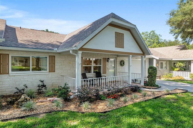 view of front of property with stone siding, covered porch, roof with shingles, and driveway