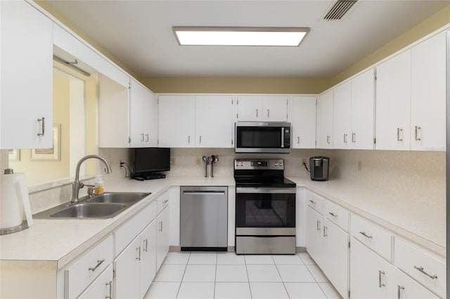 kitchen with appliances with stainless steel finishes, a sink, backsplash, light countertops, and white cabinetry