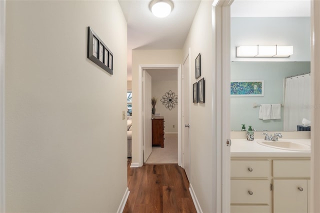 hallway featuring a sink, dark wood finished floors, and baseboards