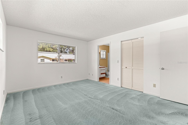 unfurnished bedroom with carpet, a textured ceiling, connected bathroom, a closet, and baseboards