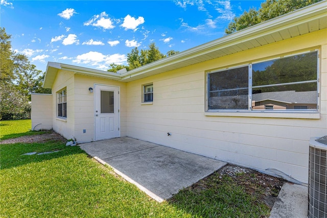 view of exterior entry featuring a yard, a patio, and central AC