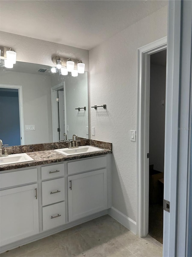 bathroom with double vanity, baseboards, and a textured wall