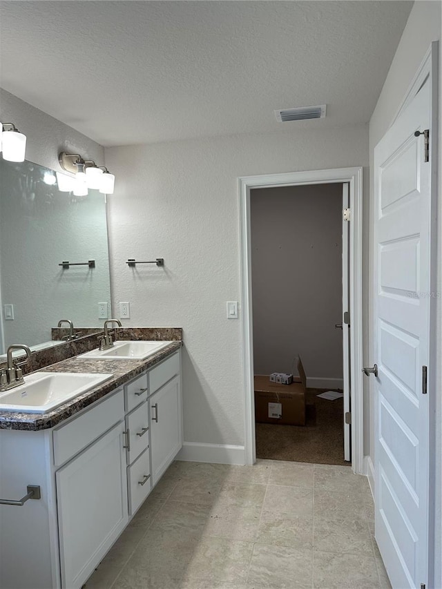 full bath with a textured ceiling, double vanity, a textured wall, and baseboards