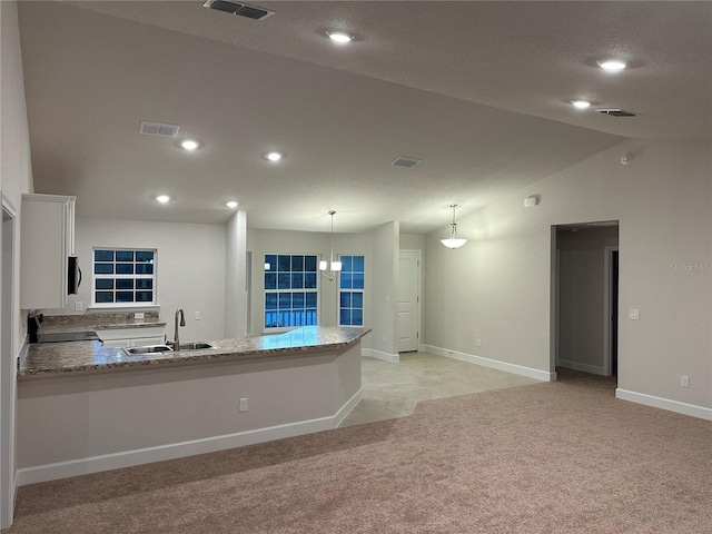 kitchen featuring a sink, light carpet, white cabinets, a peninsula, and baseboards