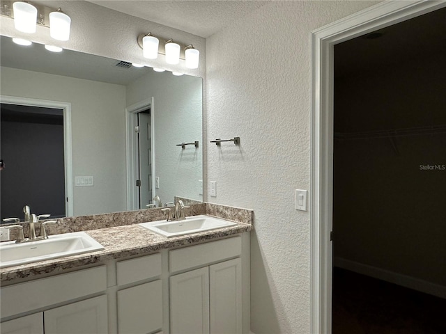 bathroom with double vanity, a textured wall, and a spacious closet