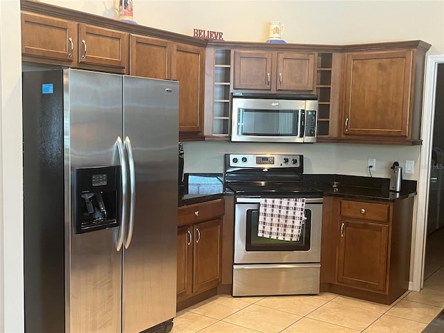 kitchen with appliances with stainless steel finishes, open shelves, light tile patterned floors, and dark stone countertops
