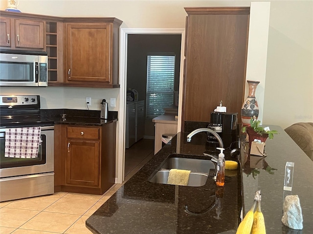 kitchen featuring appliances with stainless steel finishes, a sink, dark stone countertops, light tile patterned floors, and brown cabinets