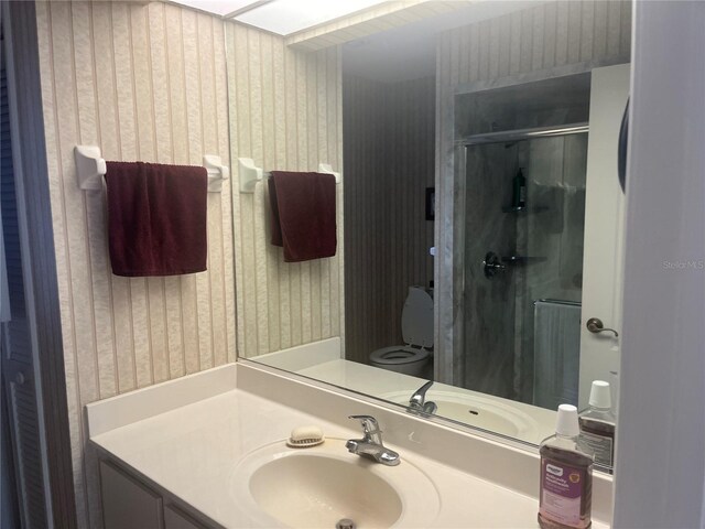 bathroom featuring wallpapered walls, a stall shower, vanity, and toilet