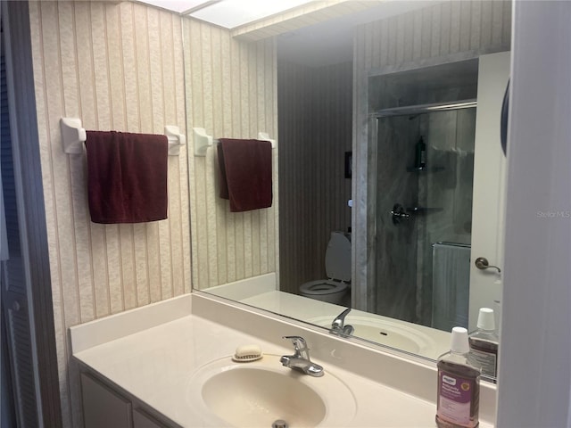 bathroom featuring wallpapered walls, a stall shower, vanity, and toilet