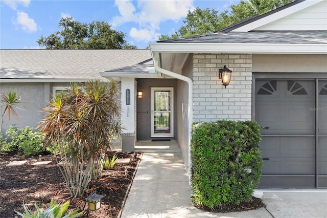 view of exterior entry featuring roof with shingles and an attached garage