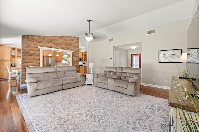 living room with wood finished floors, baseboards, wooden walls, vaulted ceiling, and ceiling fan