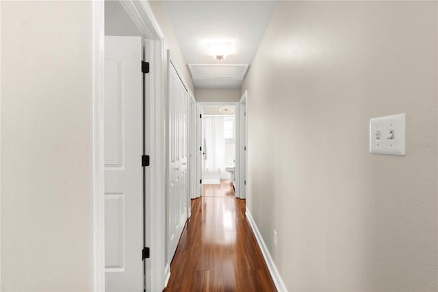 hall featuring dark wood finished floors, attic access, and baseboards