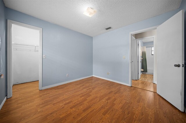 23 Larch Crse, Ocala, FL 34480 - unfurnished bedroom with a walk in closet, a closet, wood finished floors, a textured ceiling, and baseboards