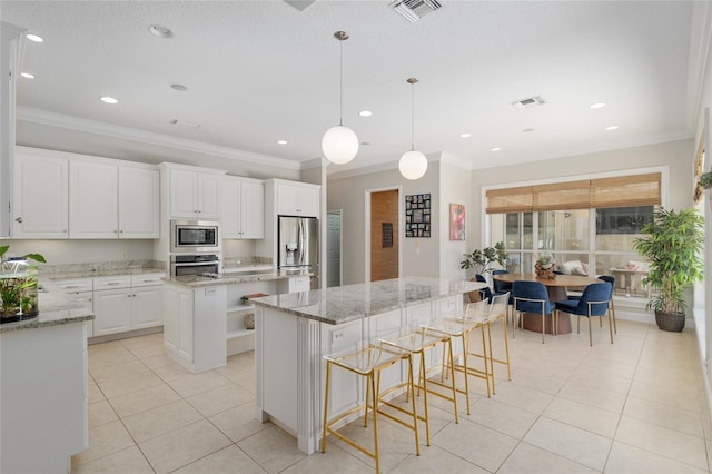kitchen with stainless steel appliances, a kitchen island, ornamental molding, light tile patterned floors, and white cabinetry